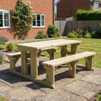 Wooden picnic table with benches on a patio in front of a brick house.